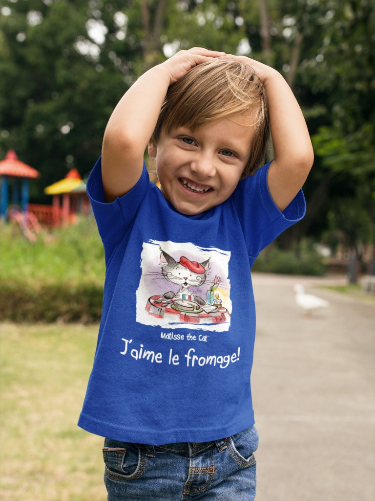A true blue official, Matisse the Cat children’s t-shirt with the slogan ‘Jaime le fromage ‘ showcases Matisse sitting at a French bistro table preparing to eat cheese. Worn by a young boy in a park smiling and holding his hands on his head.