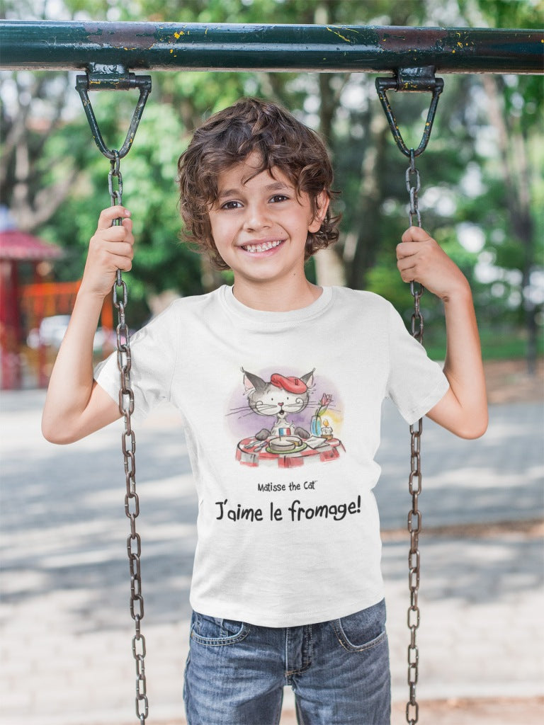 A white official, Matisse the Cat children’s t-shirt with the slogan ‘Jaime le fromage ‘ showcases Matisse sitting at a French bistro table preparing to eat cheese. Worn by a young boy on a swing.