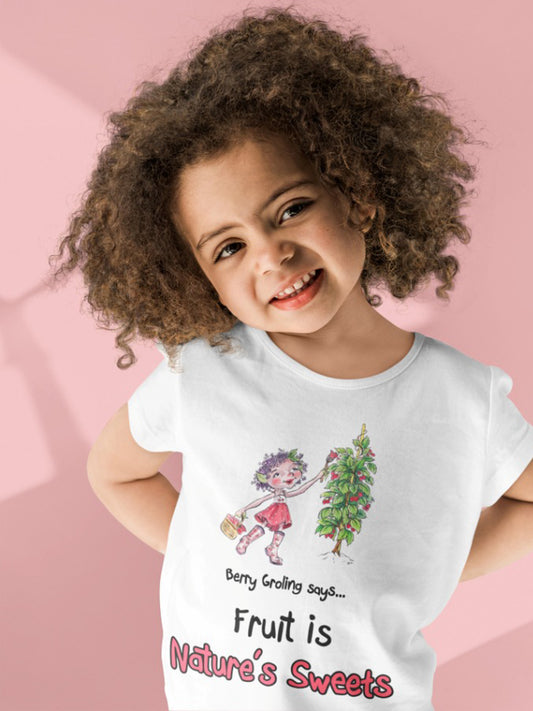 A white official Grolings kids' t-shirt, featuring the phrase 'Berry Groling says... Fruit is Nature’s Sweets'. The t-shirt showcases Berry Groling, painting sweetness into raspberries on a bush. Berry Groling is holding a basket filled with fresh raspberries, capturing the abundance and delectable sweetness of nature's bounty. The scene encourages the wearer to appreciate and enjoy the natural delights provided by the Earth. Worn by a young girl smiling and standing in front of a pink background.