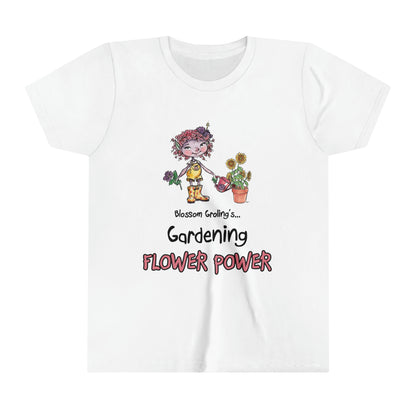 A white official Grolings kids' t-shirt, featuring the phrase 'Blossom Groling... Gardening Flower Power’. The t-shirt showcases Blossom Groling, a character from ‘Matisse and the Topsy-Turvy Farm,’ watering a sunflower plant in a pot. Blossom is holding a beautiful flower in her other hand, radiating positivity and joy. The scene encourages the wearer to embrace a positive outlook and to share kindness and optimism, much like the blossoming flowers.