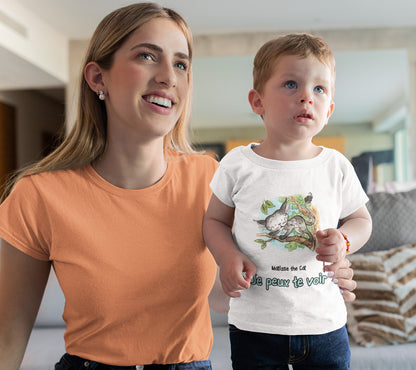 A white official, Matisse the Cat children’s t-shirt with the slogan ‘Je peux te voir’ showcases Matisse sitting in his garden smiling with a sleeping hedgehog curled up beside him resting on his leg. Worn by a young boy, standing beside his mum in a living room.