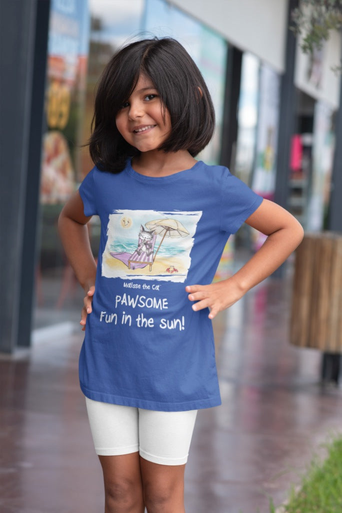 A true blue official, Matisse the Cat children’s t-shirt with the slogan ‘Pawsome Fun in the Sun ‘ showcases Matisse at the beach, relaxing on a sun lounger sipping a mile shake. Worn by a young girl standing outside a shop.