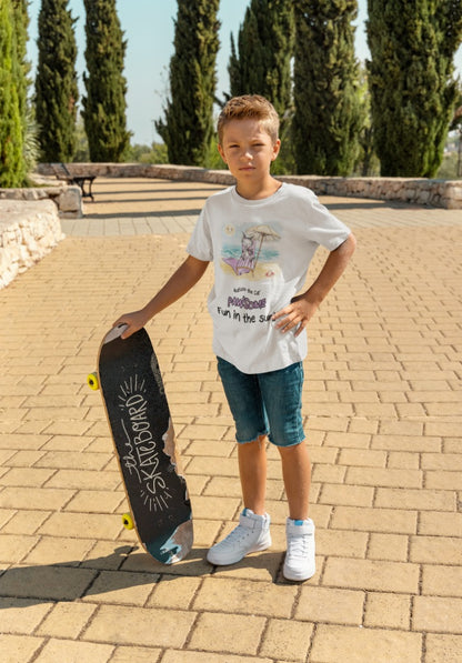 Awhite official, Matisse the Cat children’s t-shirt with the slogan ‘Pawsome Fun in the Sun ‘ showcases Matisse at the beach, relaxing on a sun lounger sipping a mile shake. Worn by a young boy standing beside his skateboard.