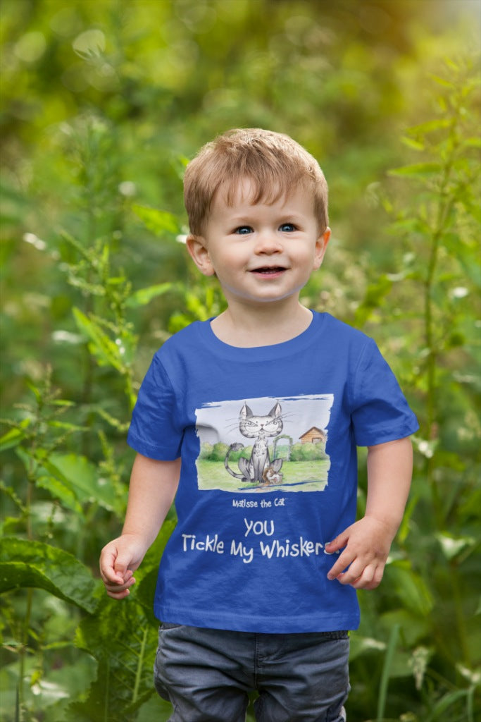 A true blue official, Matisse the Cat children’s t-shirt with the slogan ‘YOU Tickle My Whiskers ‘ showcases Matisse sitting in his garden smiling with a sleeping hedgehog curled up beside him resting on his leg. Worn by a young boy walking through foliage.