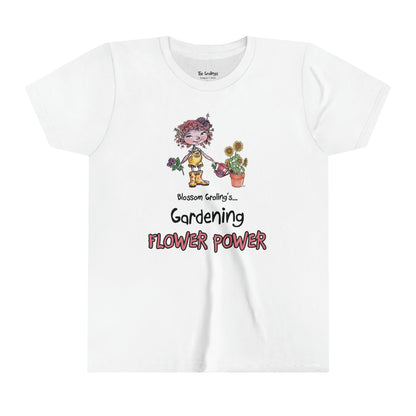 A white official USA Grolings kids' t-shirt, featuring the phrase 'Blossom Groling... Gardening Flower Power’. The t-shirt showcases Blossom Groling, a character from ‘Matisse and the Topsy-Turvy Farm,’ watering a sunflower plant in a pot. Blossom is holding a beautiful flower in her other hand, radiating positivity and joy. The scene encourages the wearer to embrace a positive outlook and to share kindness and optimism, much like the blossoming flowers.